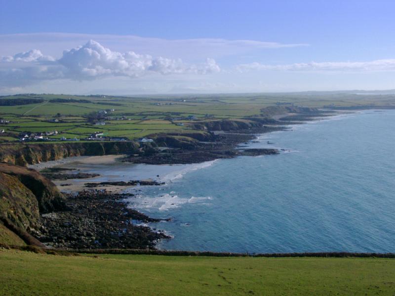 Extensive view of the Anglesey coastline and bay with a calm blue ocean, rocky cliffs and green plateau, Wales, UK