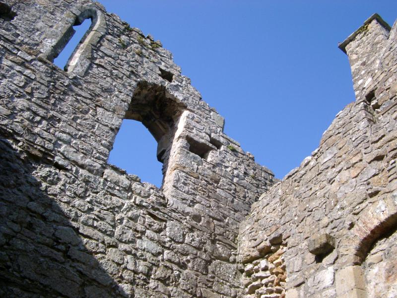 Old stone wall with window openings in a ruined building, low angle looking up against blue sky