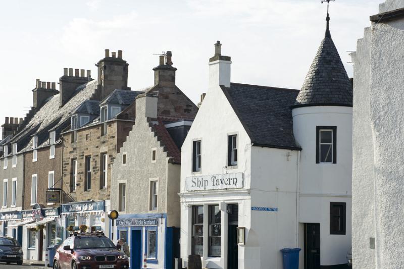 Cars parked in front of row of quaint traditional homes and storefronts in Anstruther, Scotland