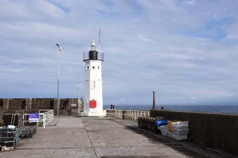 Little white lighthouse at end of pier facing ocean under partly cloudy sky in Anstruther, Scottland