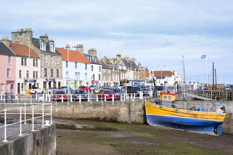 Colorful fishing boat in Anstruther harbour, Scotland beached on the sand at low tide with a view of waterfront buildings behind