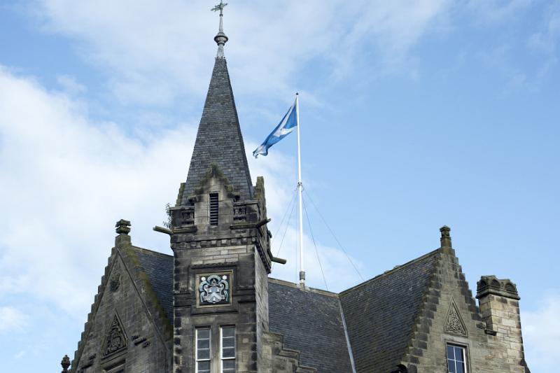 Flag on top of old weathered and stone town hall under blue sky with white clouds in Saint Andrews Scotland