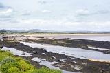 Low tide with seaweed covered rocks under partly cloudy sky with mountains at far background in Saint Andrews, Scotland