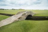 Picturesque old stone Swilken Bridge connecting the fairways on St Andrews gold course in St Andrews, Scotland under a grey cloudy sky