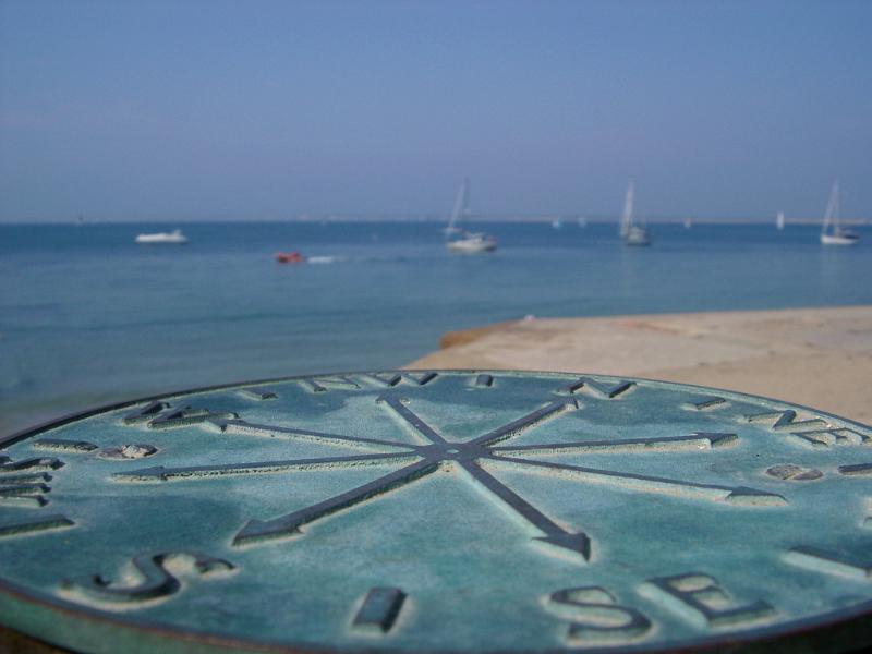 metal plaque marking the points of the compass with yachts on the water in the background