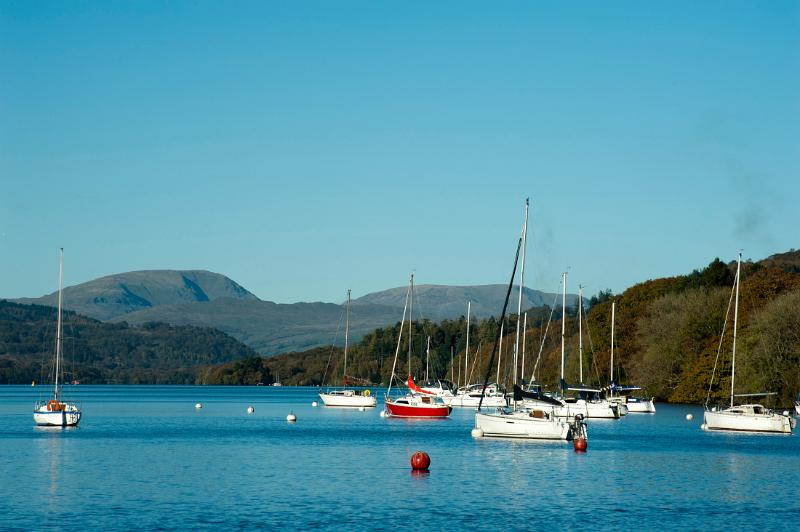 Yachts moored to buoys on the calm water of the lake at Windermere in the Lake District in Cumbria