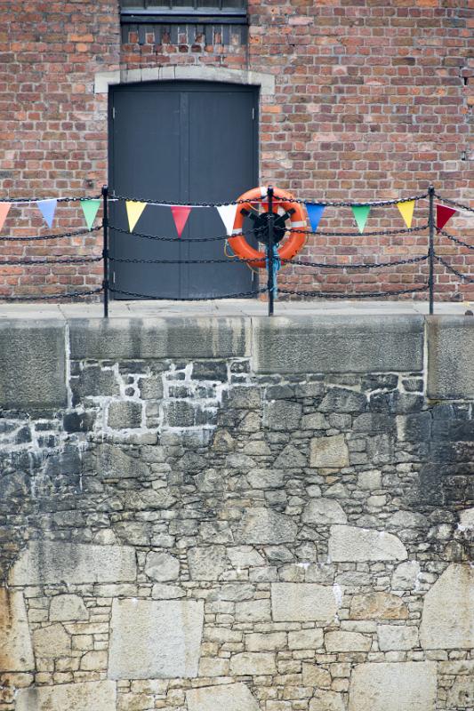 Orange life preserver on iron pole and chain railing at Liverpool Albert Dock with locked black doors surround by brick wall