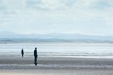 Pair of solitary life size Another Place statues made by Antony Gormley facing water in Crosby, United Kingdom