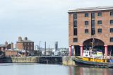 Waterfront view of a quay at Albert Dock, Liverpool, England with an old boat moored alongside, pedestrians and the city skyline behind