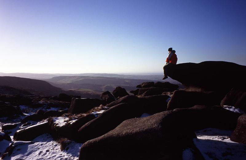 Person enjoying the tranquility of nature sitting on a rock on a snowy winter Kinder Scout, a moorland plateau and National Nature Reserve in the Dark Peak of the Derbyshire Peak District in England