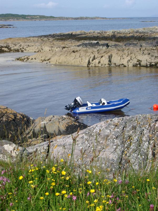 Inflatable rubber dinghy with a small outboard engine moored to a buoy in a rocky coastal inlet in Maillag, Scotland