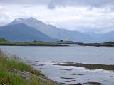 Scenic view across the water of the Isle of Skye and its lighthouse below mountain peaks on a sunny cloudy day