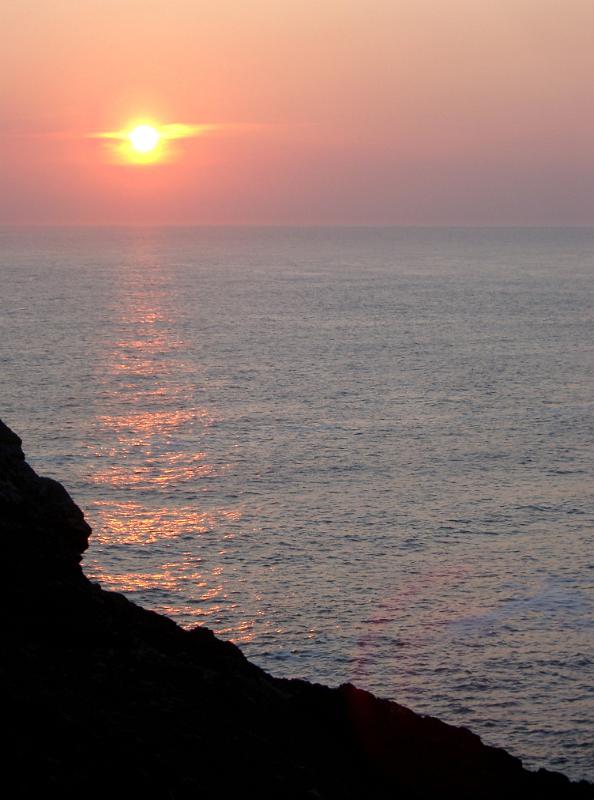 Fiery ocean sunset Fiery ocean sunset with the bright glowing sun surrounded by a halo casting a beam across the water to a silhouetted cliff on the Scottish coast