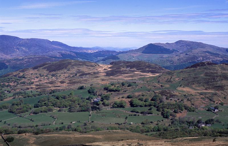 Panoramic Welsh landscape with rolling hills and distant purple mountain ranges under a blue sky