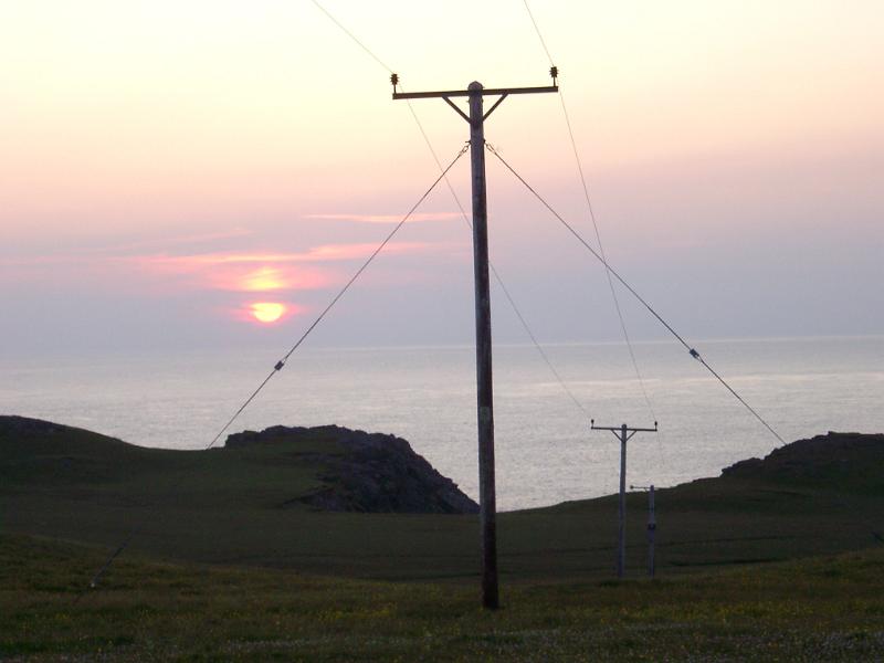 Power and telecommunications lines on poles silhouetted against a colorful sky in Scotland at sunset