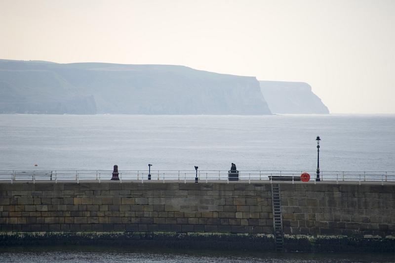 a view across one of the stone piers at whitby an the coastal headlands beyond