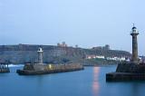 a still dusk over whitby lower harbour, with the piers, lighhouses, fishermans cottages and the abbey on the hill in view
