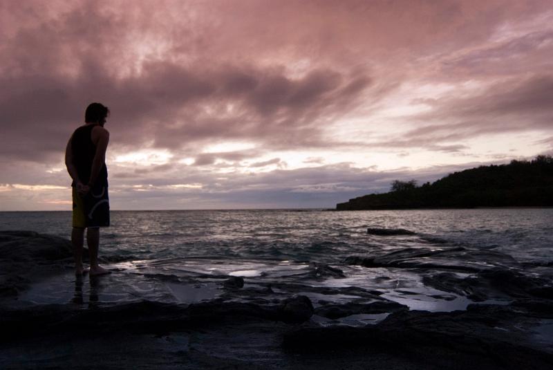 Man watching a marine sunset Man in silhouette standing on the seashore watching a marine sunset with clouds tinted a lilac purple