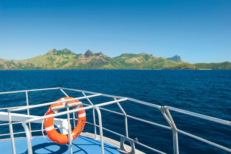 Fiji Island Transfer Life ring on the railing of a boat cruising out at sea with Way island in Fiji in the background