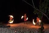 Three Fijian men performing a fire dance on the beach twirling flaming branches in the night sky
