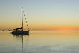 sunset over calm tropical waters with the silhouette of a sailing yacht