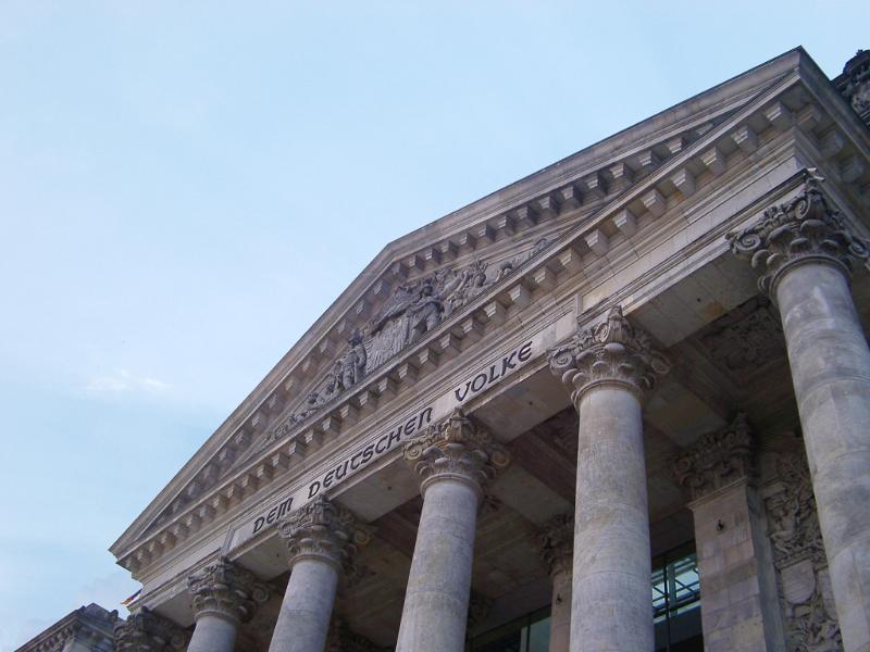 Front facade of the Reichstag building in Berlin showing the stone inscription and pillared portico, the seat of government and a popular tourist attraction