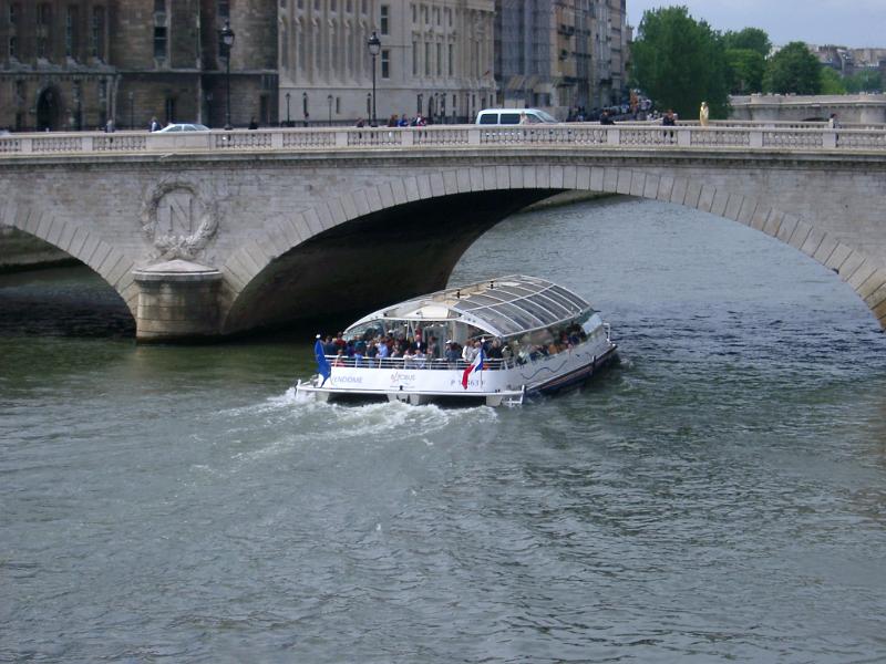 Tour boat or ferry passing under a bridge with traffic on the River Seine in Paris