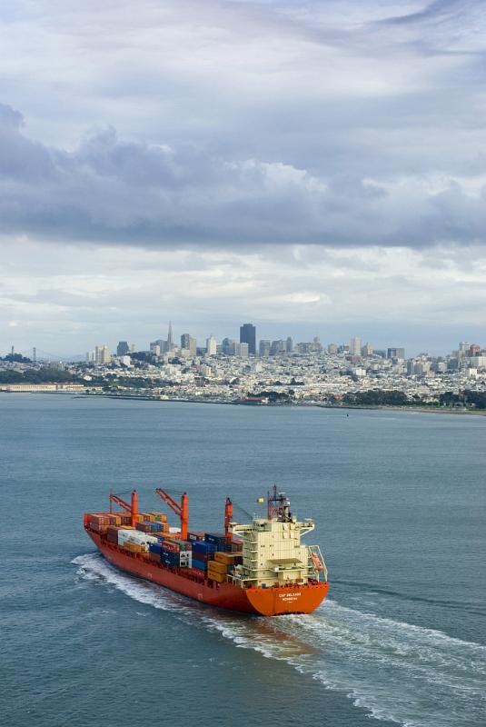 Container ship entering San Francisco bay laden with international cargo containers with the city skyline in the distance