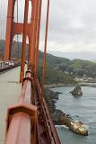 Walk along the Golden Gate Bridge on the pedestrian footpath with a view along the red painted railing with the rocks and bay below