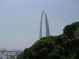 Famous St. Louis Gate Way Arch in Side View Surrounded by Green Trees on Light Blue Gray Sky Background.