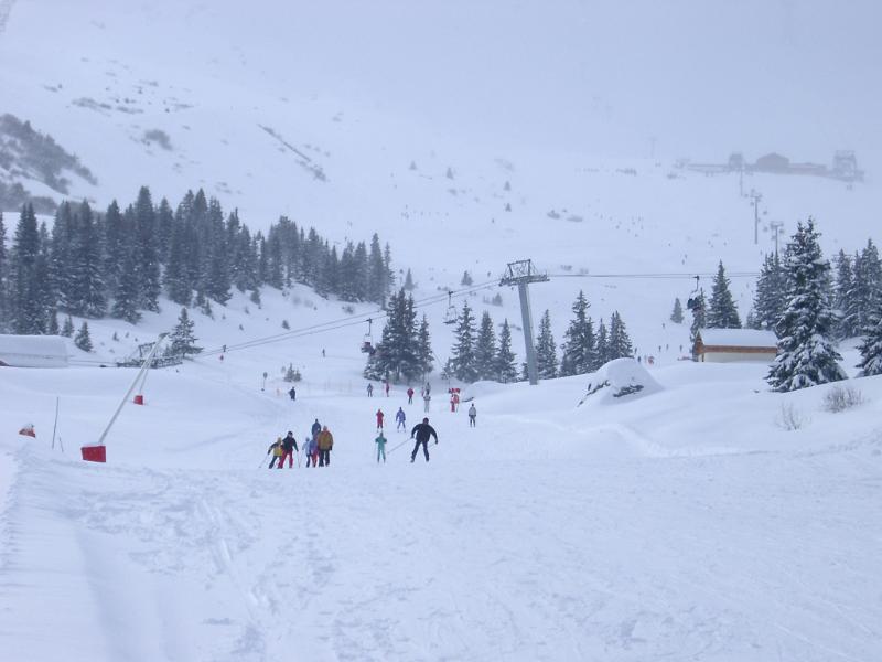 Group of independent skiers on a broad fresh piste dotted with fir trees at a mountain resort with chair lift for access to the slopes, scenic winter landscape