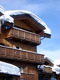 Snow Covering Rooftop of Vintage Wooden Alpine Lodge on Lighter Blue Sky Background.