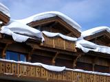 Detail of the roof and balconies of a traditional wooden alpine lodge covered in snow against a sunny blue sky