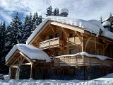 Scenic view of a traditional wooden snow covered alpine lodge set amongst evergreen fir trees in a steep mountain valley