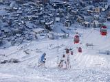 View looking down the piste of a chair lift and snowy alpine village or resort with skiers in winter