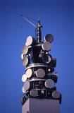 Telecommunications tower with dishes and antennae for reception and broadcasting of wireless radio waves against a clear blue sky