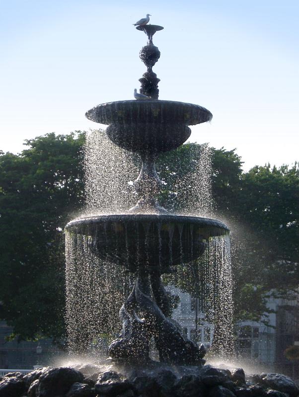 Ornamental Brighton stone fountain with falling curtains of water and pigeons enjoying the cool spray on a hot day