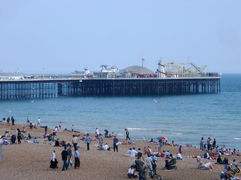 View from the beach of Brighton pier with its amusement arcade and historical buildings which are a popular tourist venue, people in the foreground on the sand