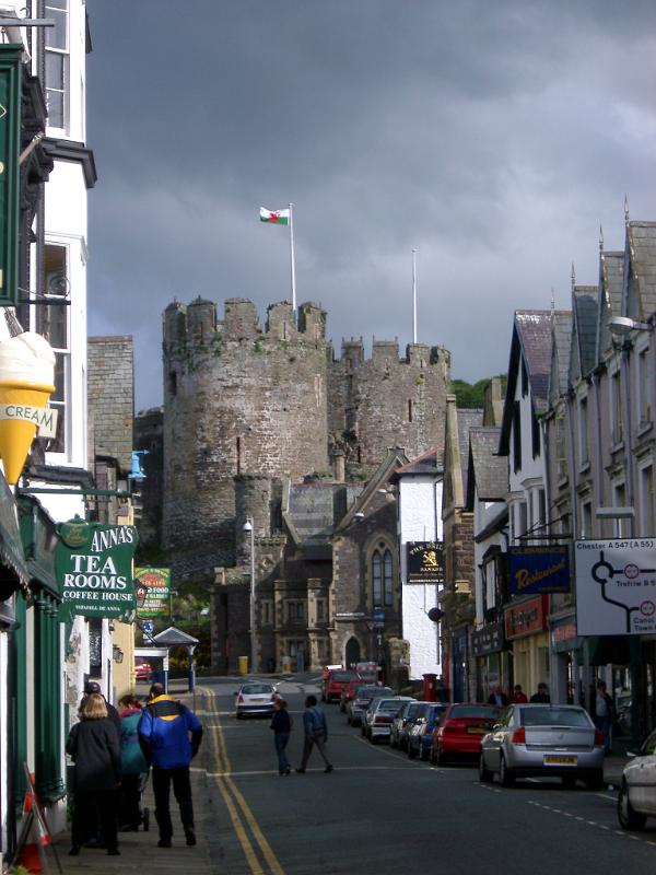 Busy Street Scene with Vehicles and People at Conwy, Wales. Captured with the Castle on a Stormy Sky Above.