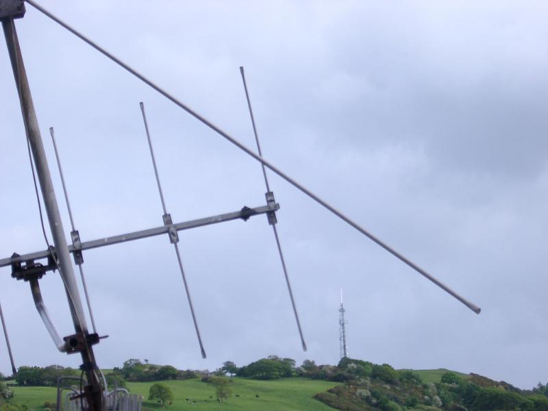 TV Antenna and receiver for communications and broadcast silhouetted against a hazy blue sky in rural countryside in Wales