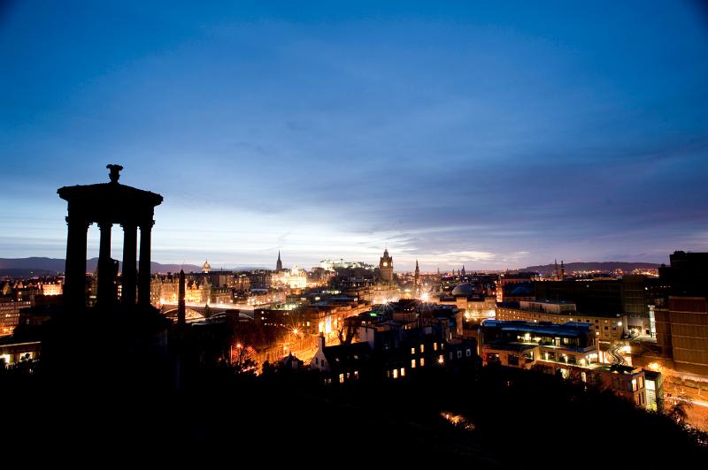 Silhouette of the Dugald Stewart Monument on carlton hill with a panoramic view of edinbrugh at night behind