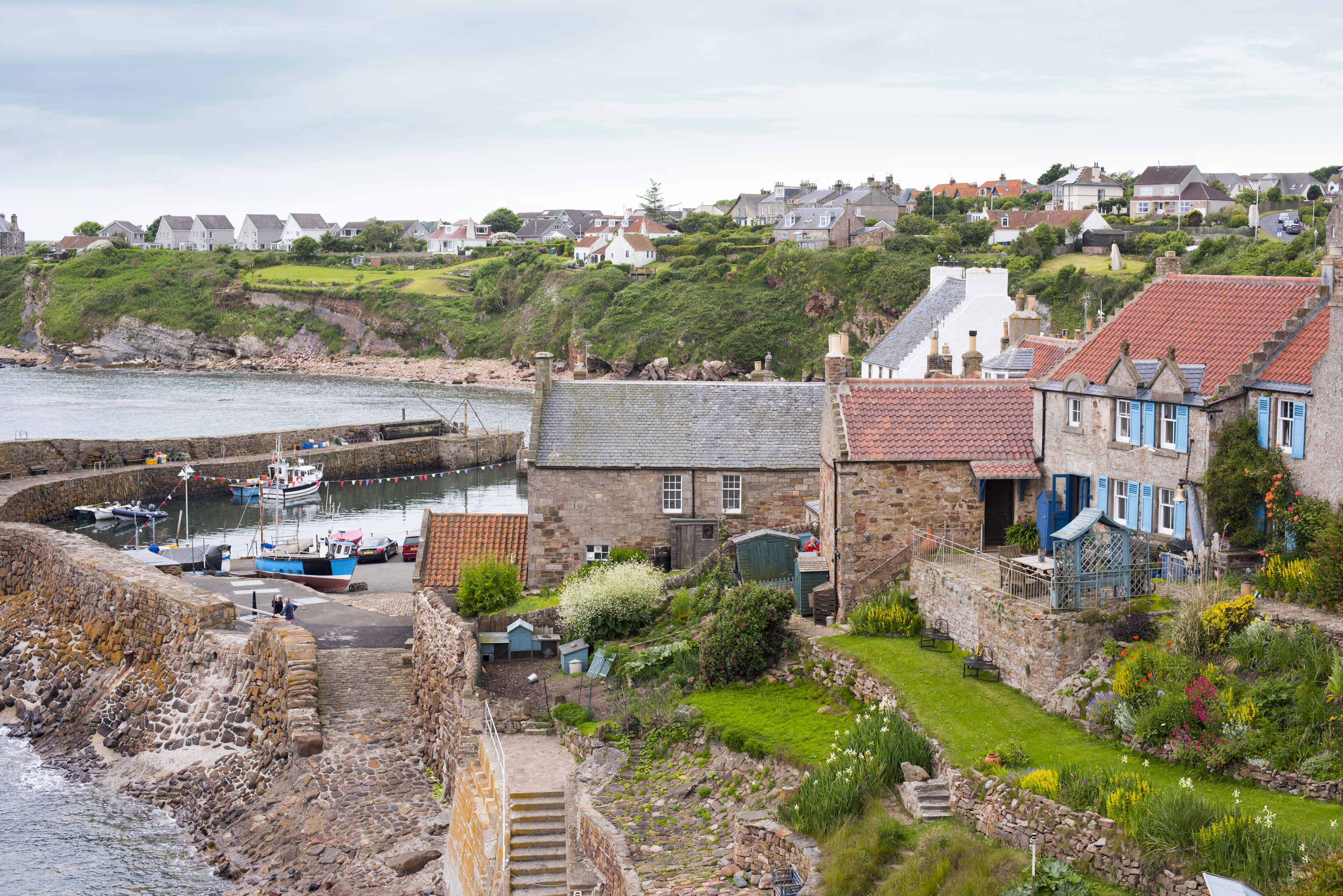 an image of View of quaint houses, boats in bay and stairway down to water in Crail on the Fife Coast in Scotland
