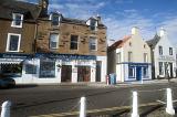 Street scene in Anstruther, Scotland with a view of shops and apartments on a main road with bollards in the foreground