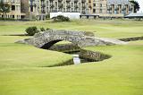 Picturesque view of the stone Swilken Bridge on St Andrews golf course, Scotland spanning a meandering stream between fairways with the town in the background