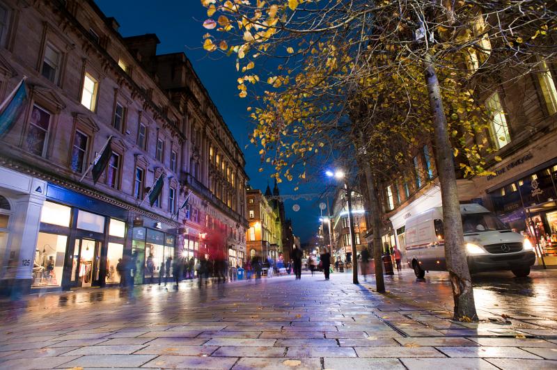 Colourful night scene in Buchanan St, Glasgow with illuminated lights in the retail shops and pedestrians walking about