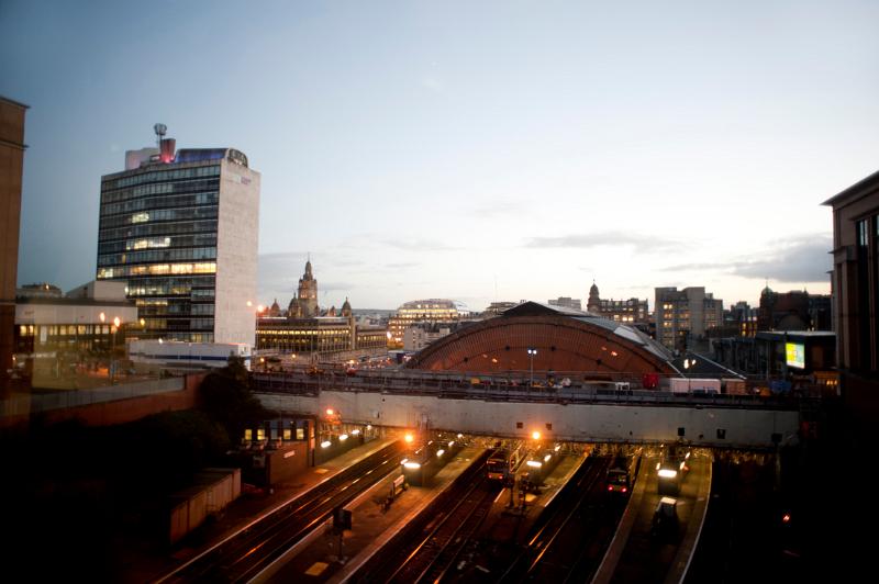 High angle view of Glasgow Queenstreet Station at night with four illuminated trains waiting for passengers at the covered platforms and a view over the rooftops of the city beyond