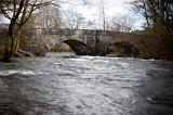 View of a fast flowing river in spate passing under the old stone arches of Skelwith Bridge in the Lake District in Cumbria