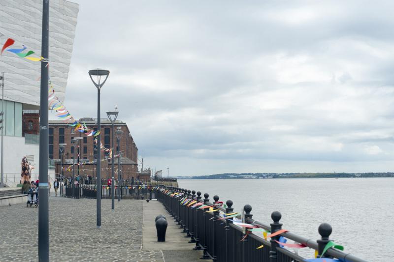 Cobbled promenade at Liverpool Mersey waterfront with colorful bunting on the street lamps and railing leading to the historical buildings in the background, Liverpool, England