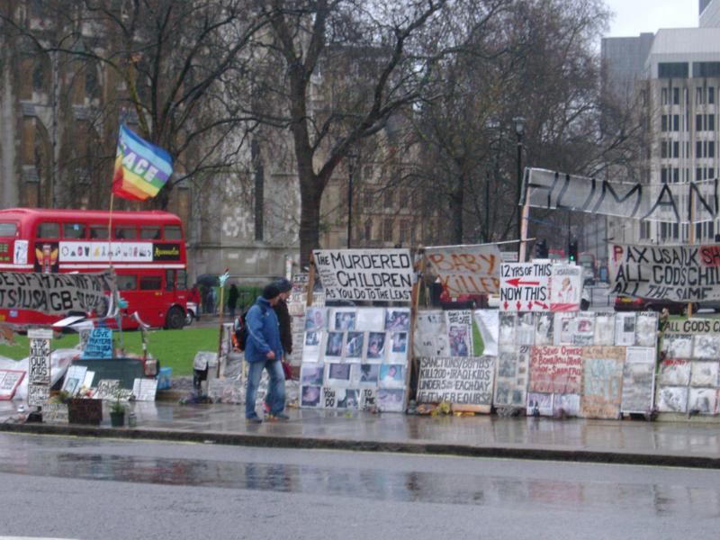 Streetside demonstartion in London with a pedestrian walking past a display of placards and slogans on a wet rainy day