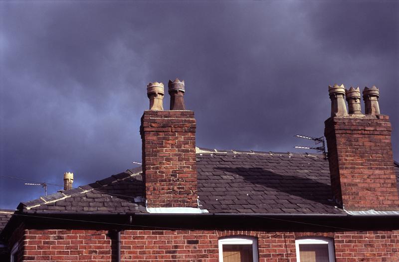 Red brick chimney pots on old terraced houses in Stockport against an ominous cloudy sky